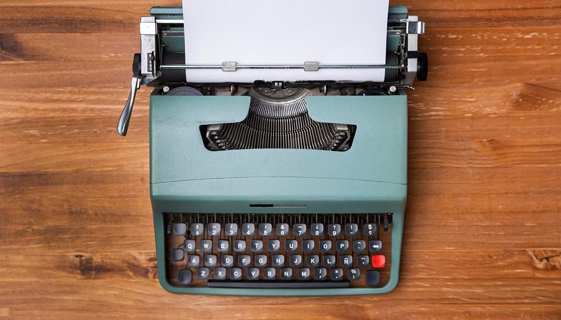 Vintage typewriter with a blank sheet on a wooden desk