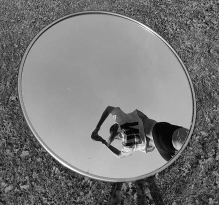 Person photographing their reflection in a round mirror lying on the grass